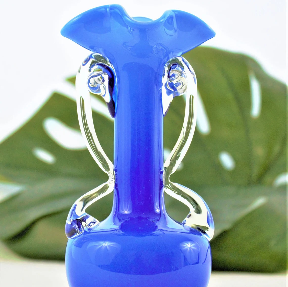 Blue glass vase with clear base against a green leaf background
