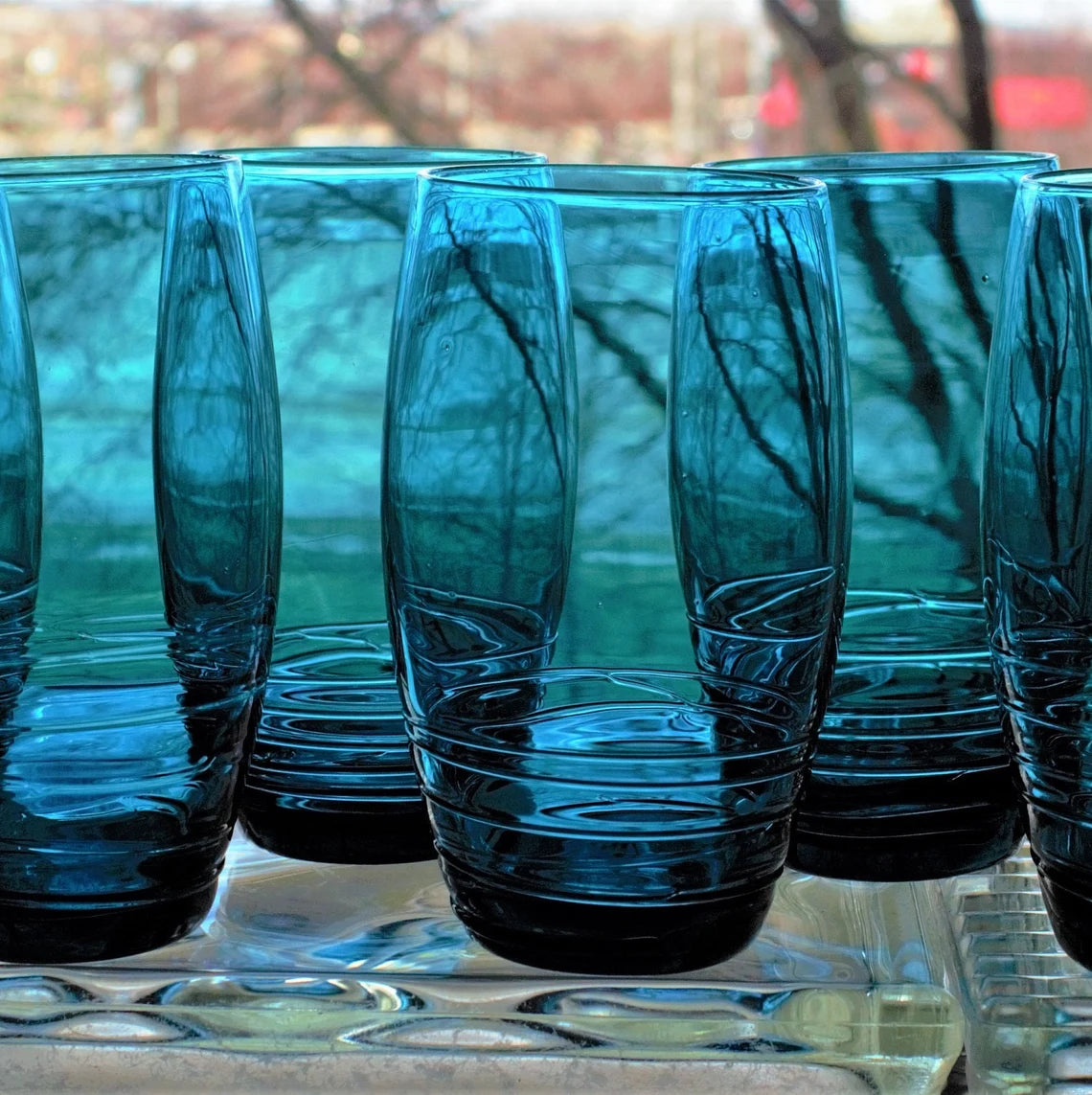 Set of blue glass tumblers on a reflective surface with blurred natural background
