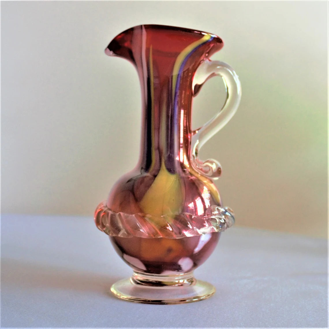 Pinkish glass pitcher on a white surface with a light background