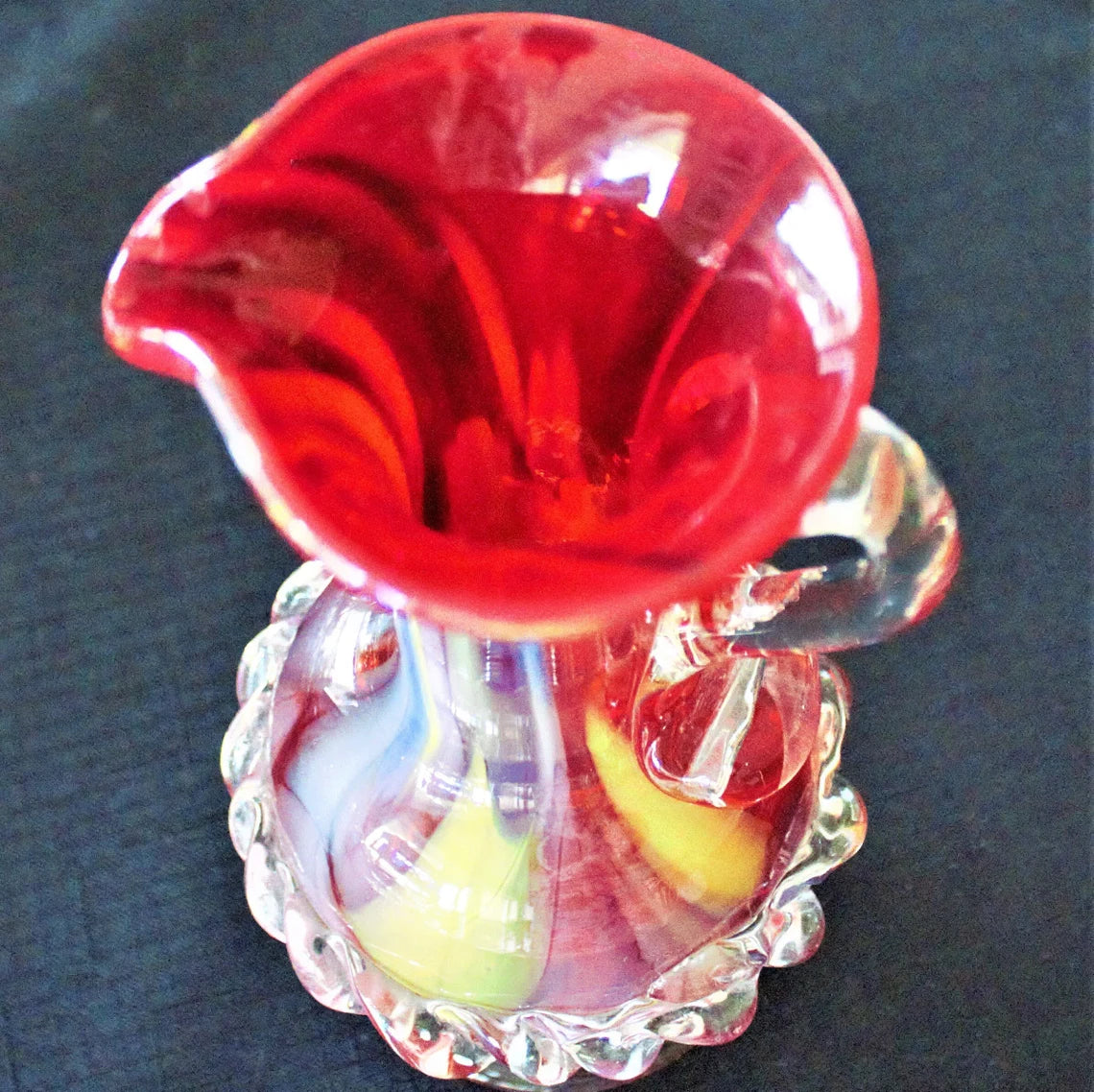 Glass sculpture with a red flower-like top and colorful base on a dark background