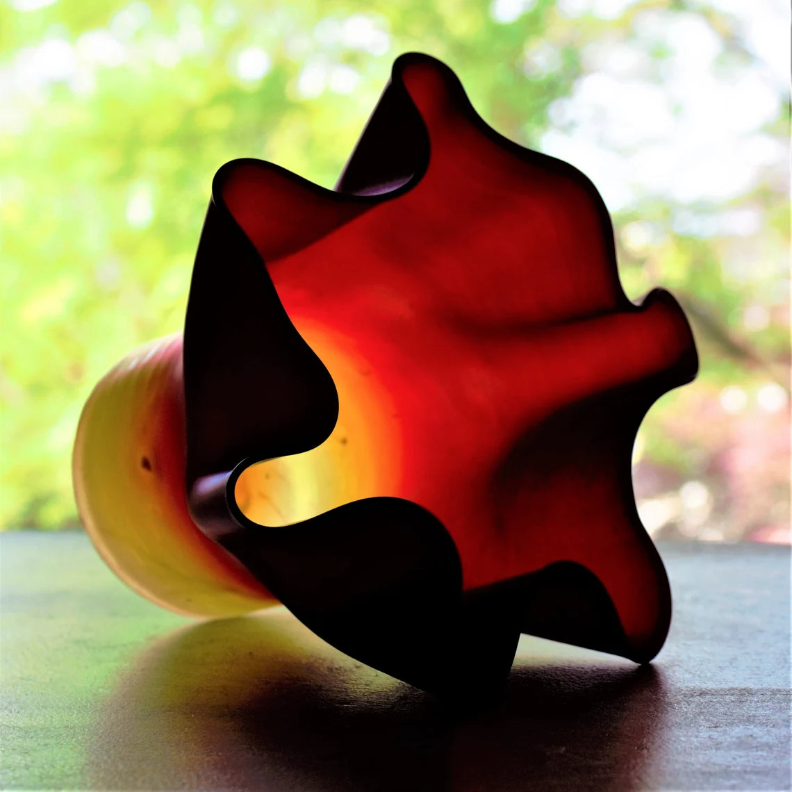 Colorful glass vase on a reflective surface with a blurred natural background