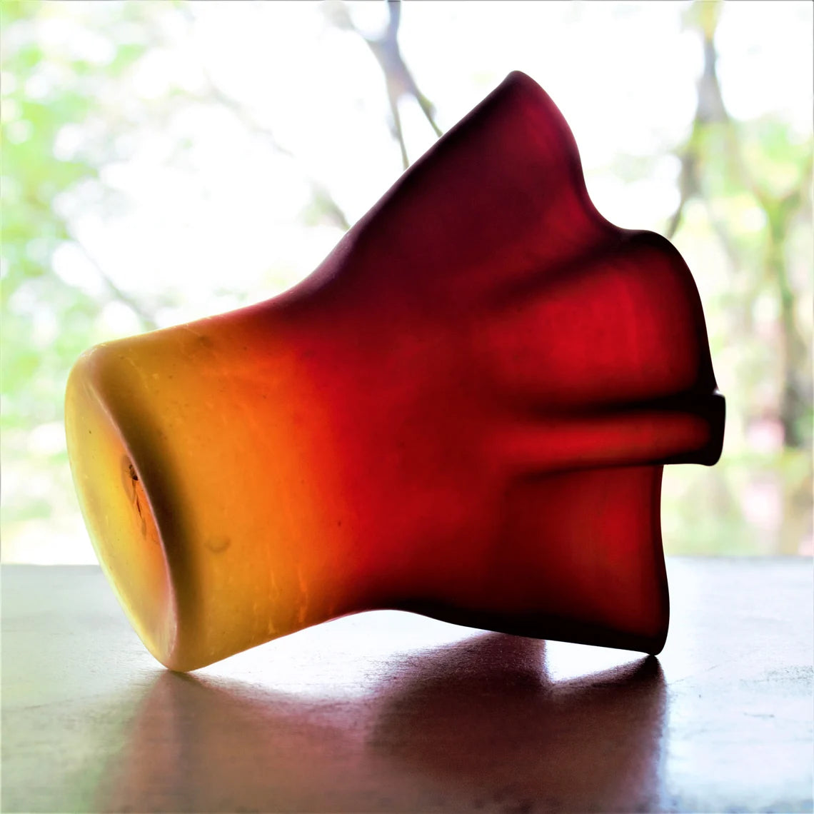 Glass vase with a gradient color from red to yellow on a reflective surface.