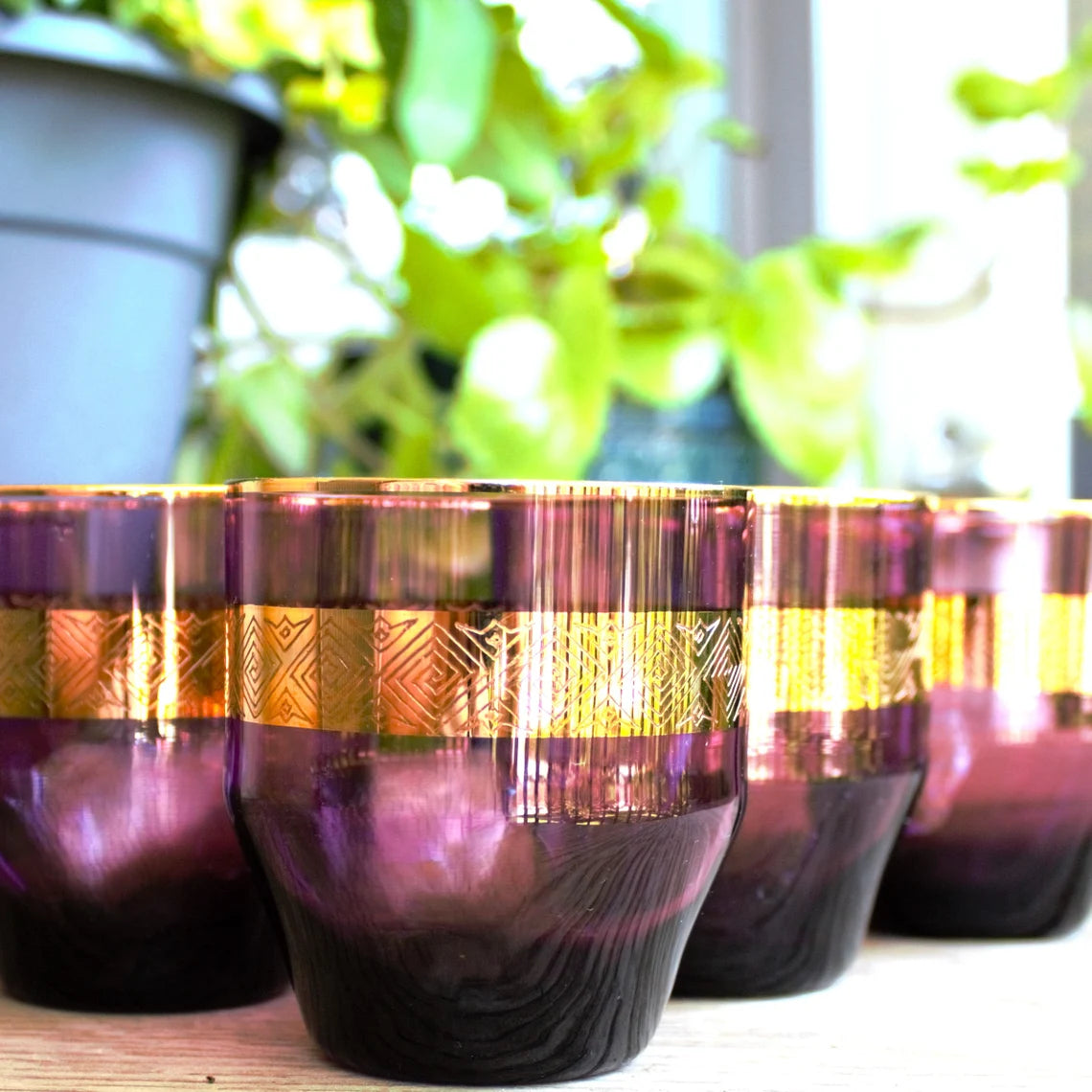 Decorative purple and gold tumblers on a surface with plants in the background