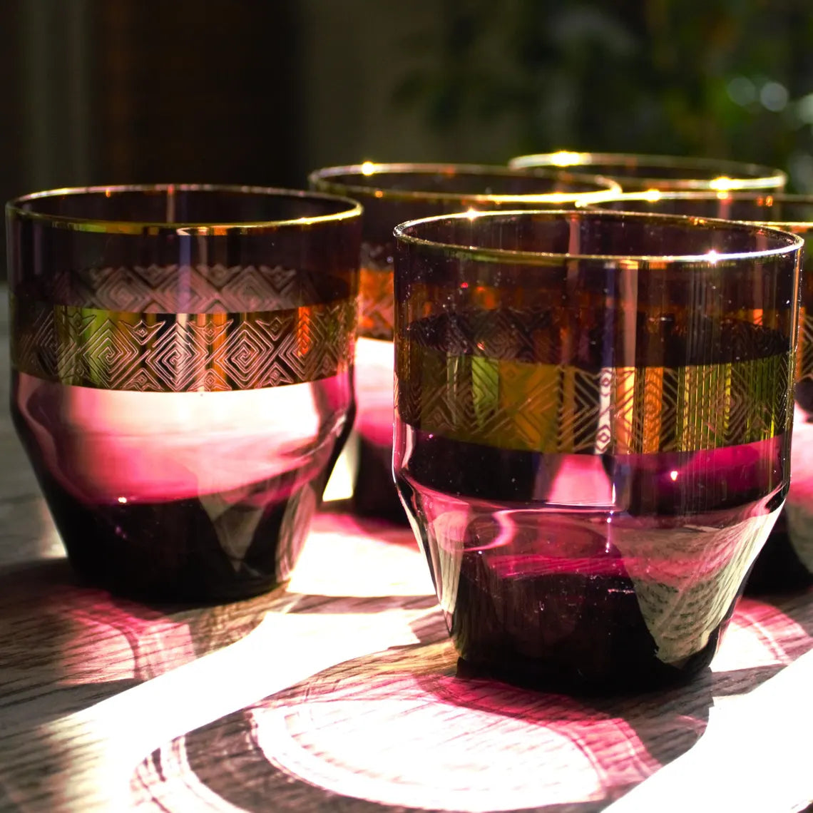 Set of four decorative glasses with gold and purple patterns on a reflective surface.