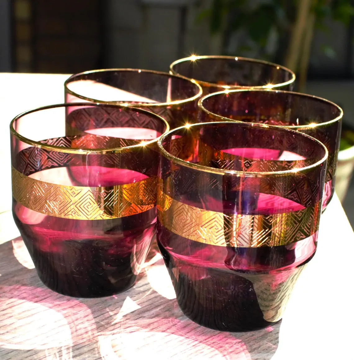 Set of six purple glasses with gold accents on a tablecloth.