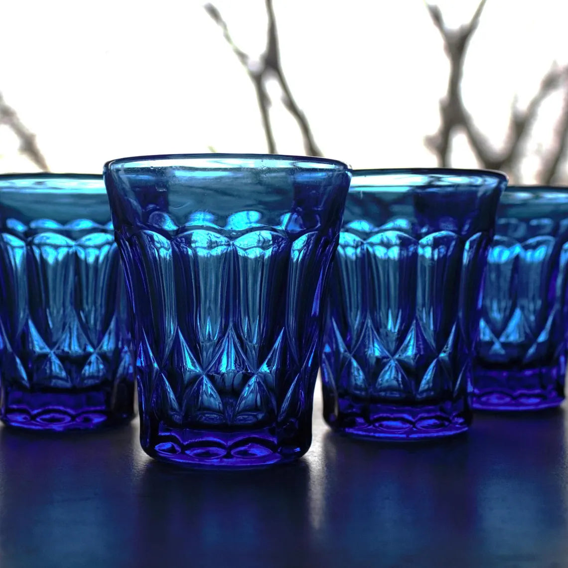 Set of four blue glass tumblers with textured design on a dark surface.