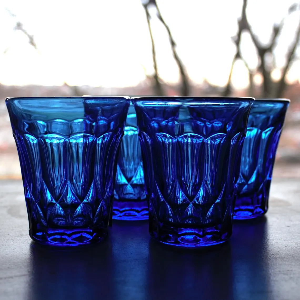 Set of blue glass tumblers on a wooden surface with a blurred natural background