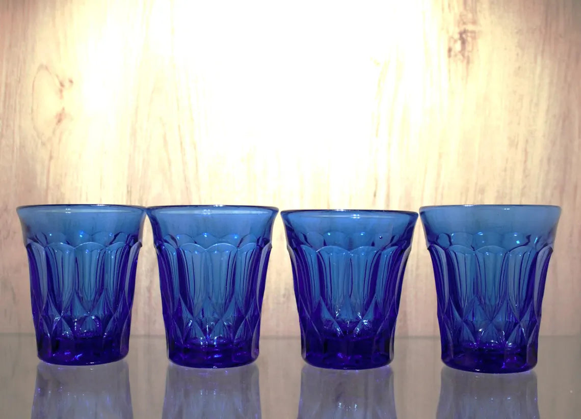Four blue glass tumblers with a textured design on a reflective surface.