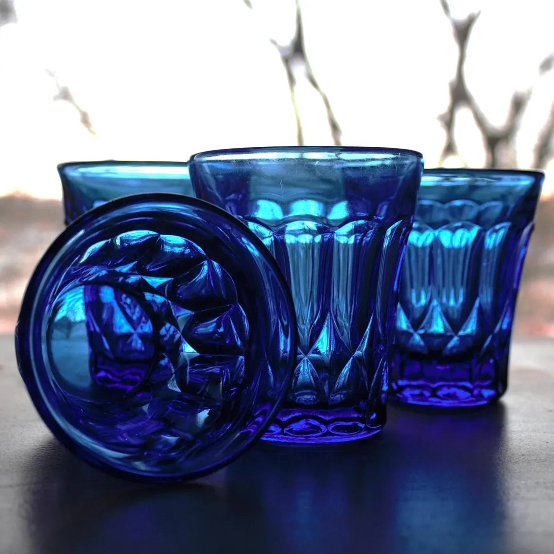 Set of blue glass tumblers with textured design on a reflective surface.