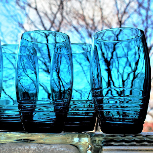 Set of blue glass tumblers on a reflective surface with blurred natural background