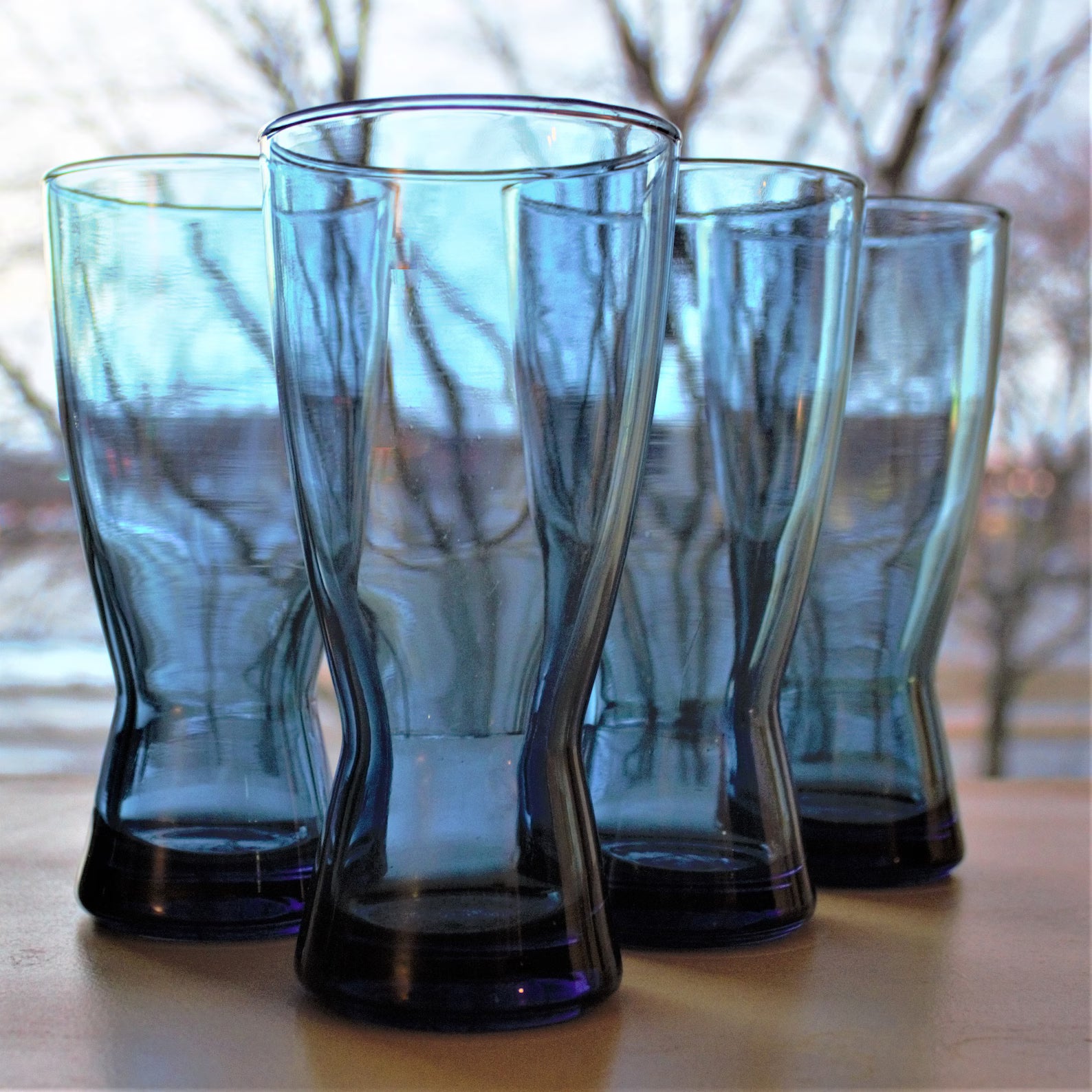 Set of four blue glass tumblers on a wooden surface with a blurred natural background