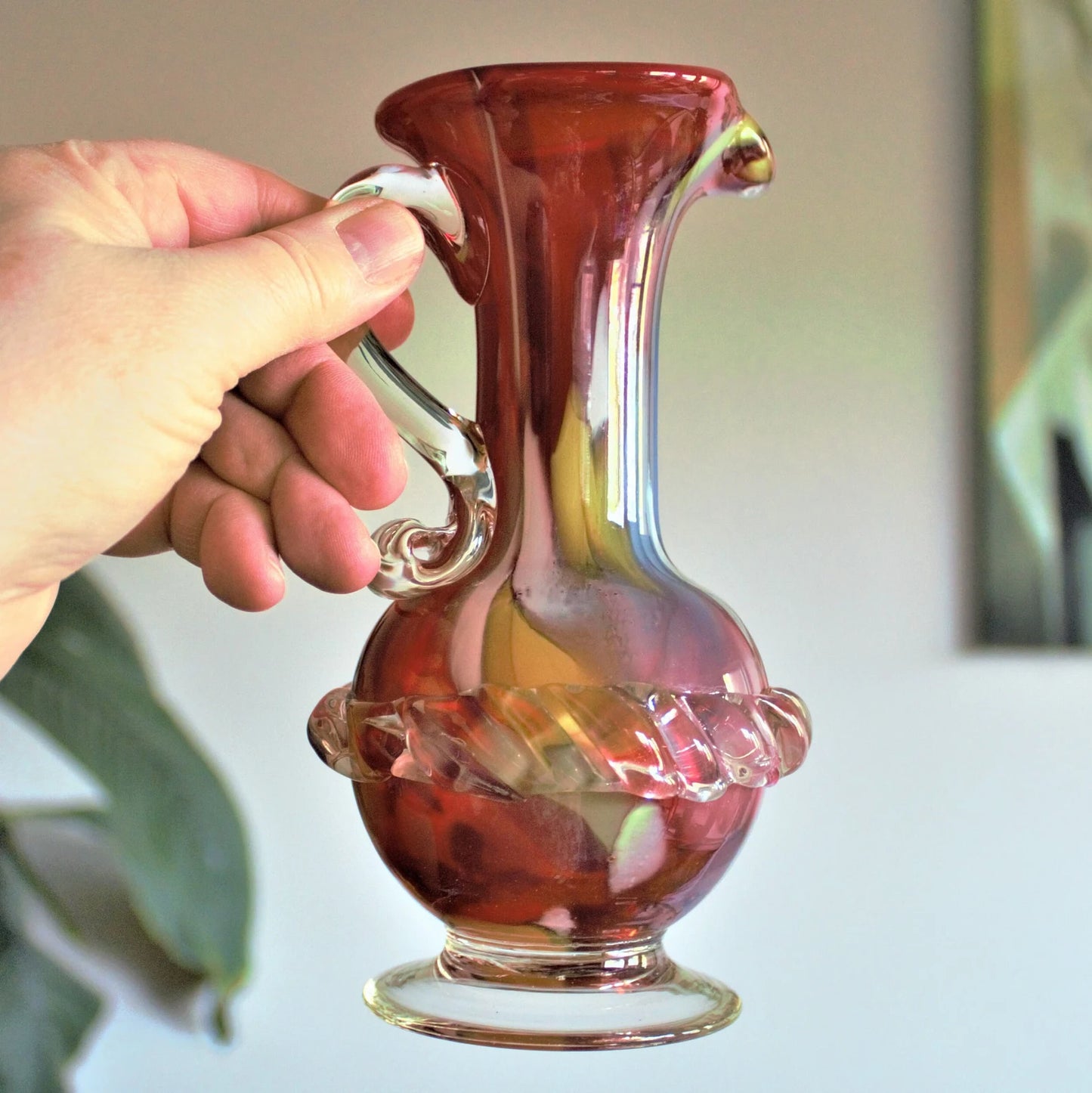 Hand holding a decorative glass pitcher with a blurred background
