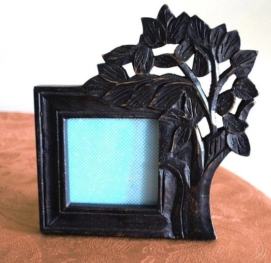 Decorative black photo frame with leaf design on a wooden surface