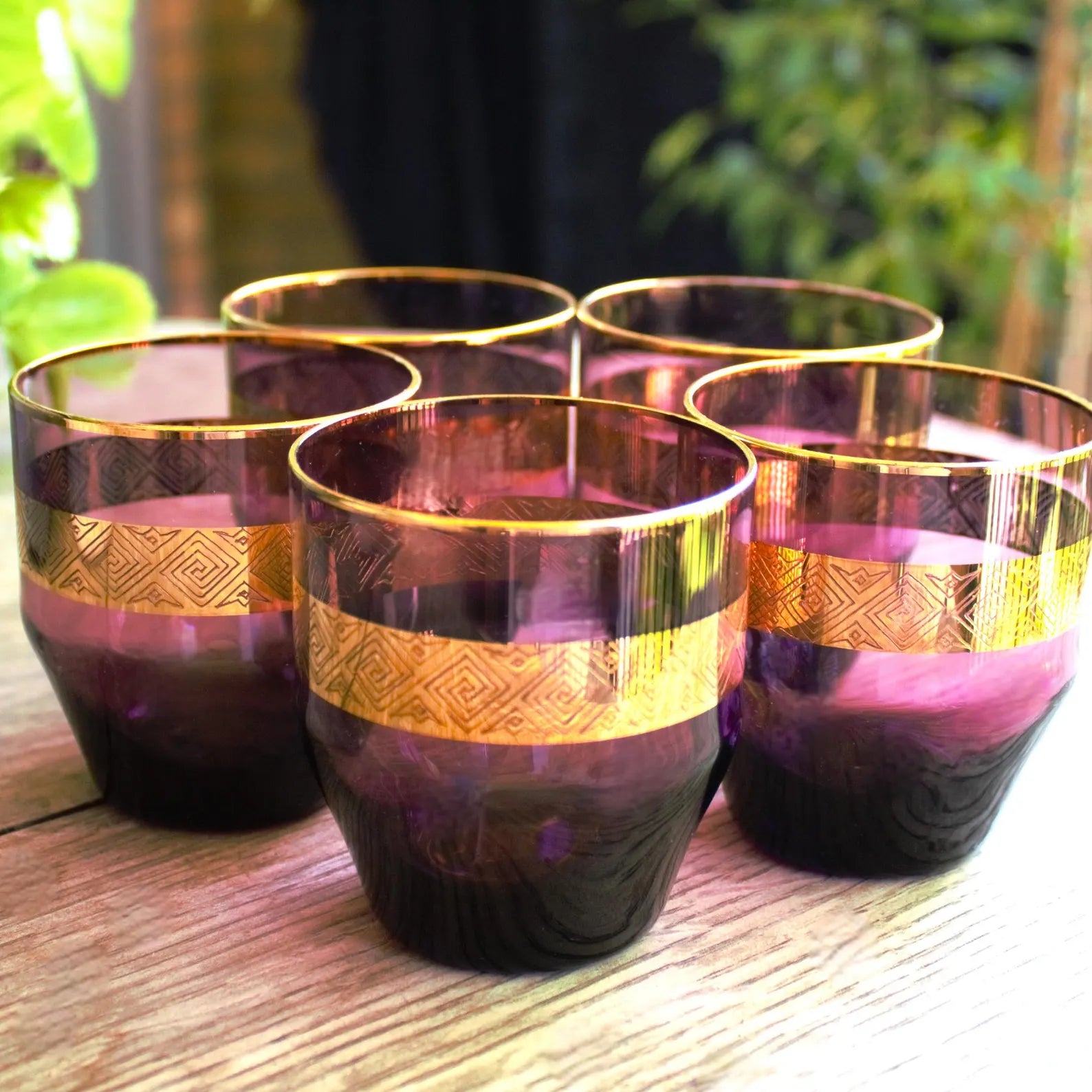 Set of four purple glasses with gold bands on a wooden surface