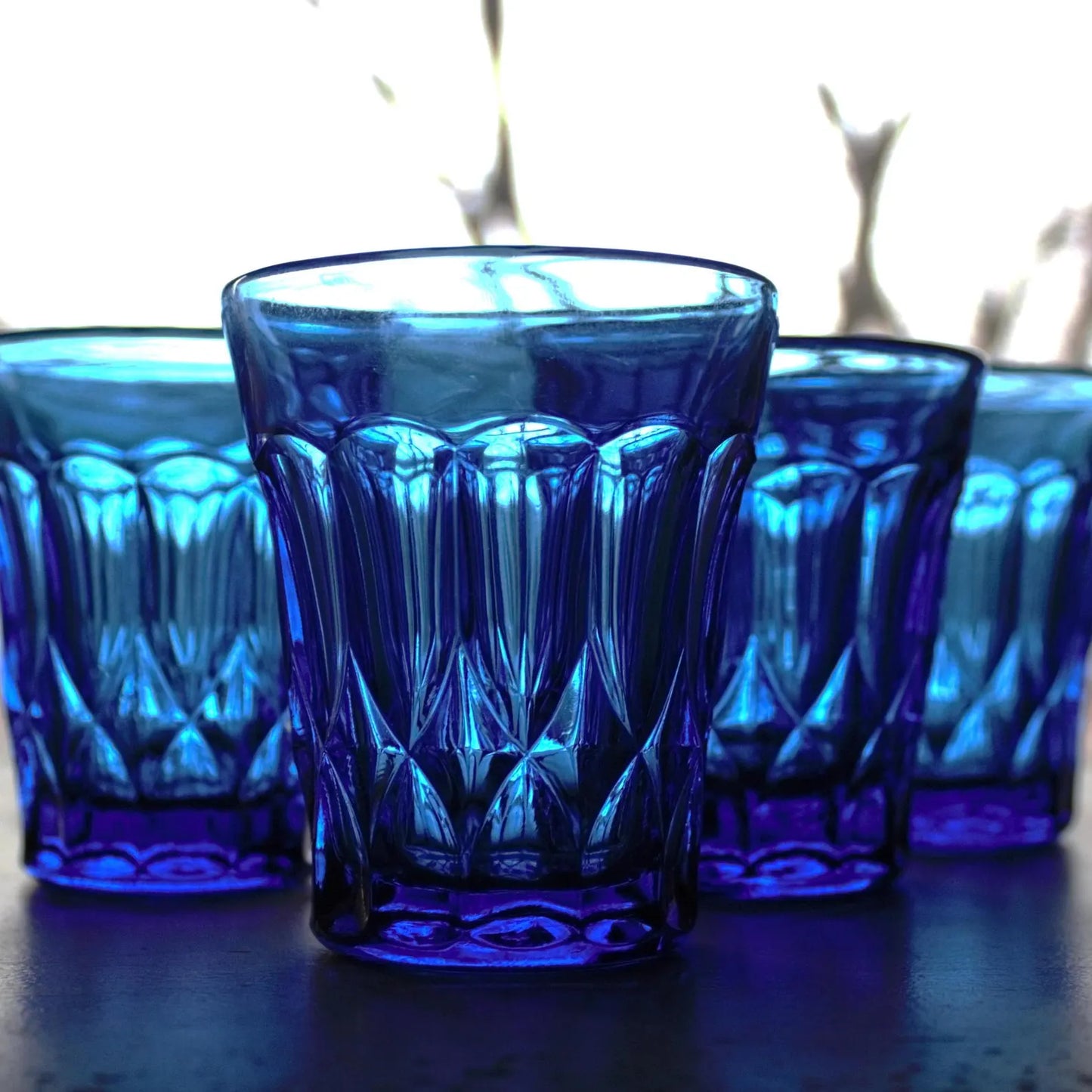Set of blue glass tumblers with a textured design on a dark surface.